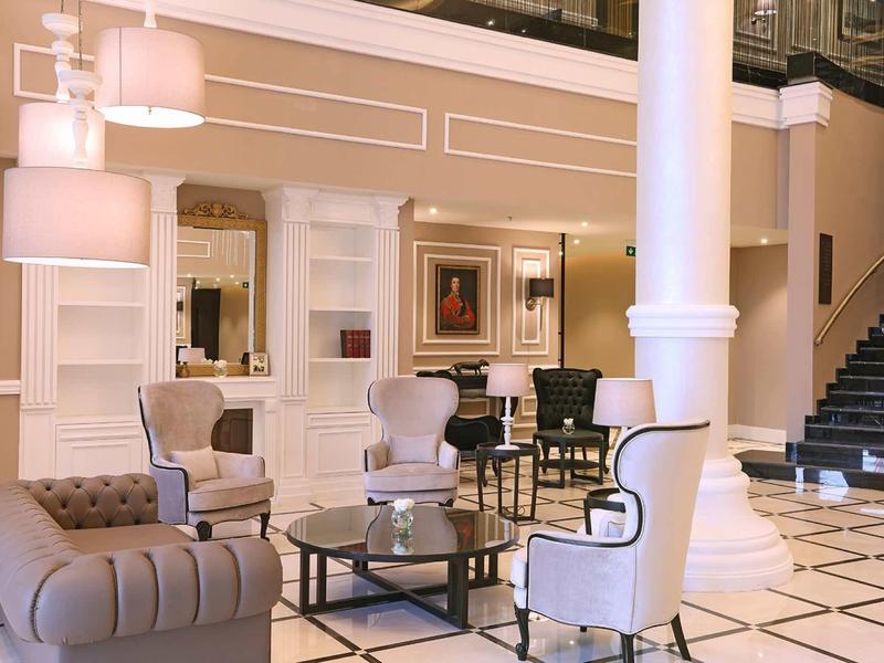 Elegantes Wohnzimmer mit weißen Wänden, schwarzen Treppen, Sesseln und Glastischen auf Kachelboden.