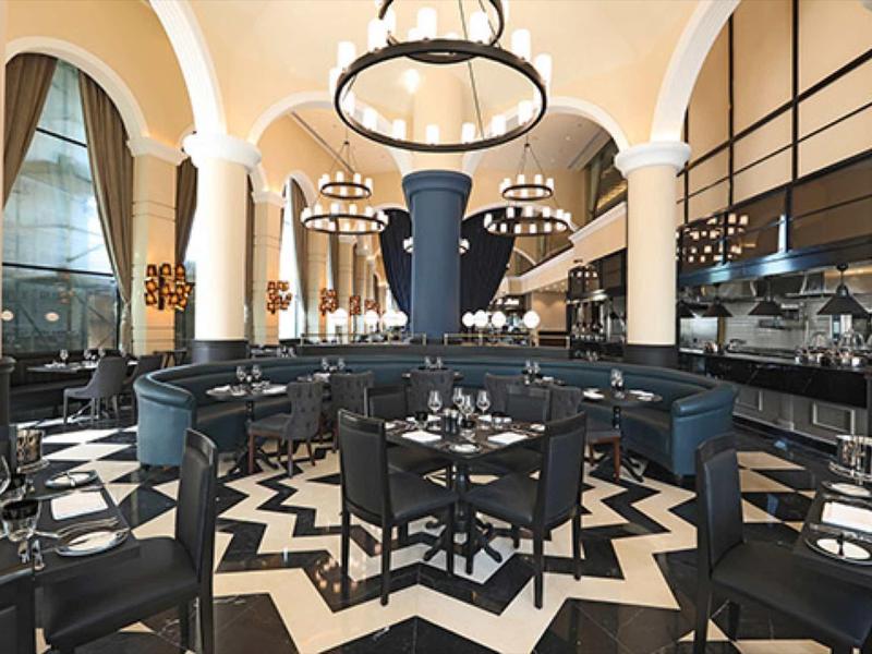 Elegantes Restaurant mit hohen Bögen, schwarzer Polsterung, runden Lampen und schwarz-weißem Boden.