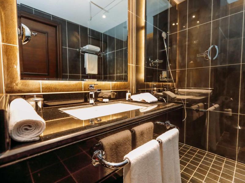 Modernes Badezimmer mit großen braunen Fliesen, beleuchtetem Spiegel und weißem Waschbecken.