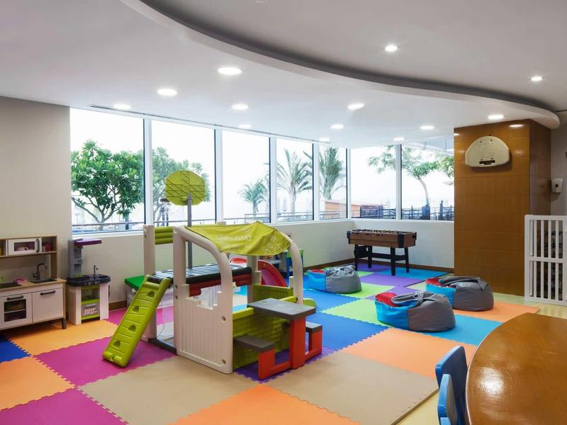 Bunter Kinderspielraum mit Teppichfliesen, Spielzeug, Klettergerüst und großem Fenster.