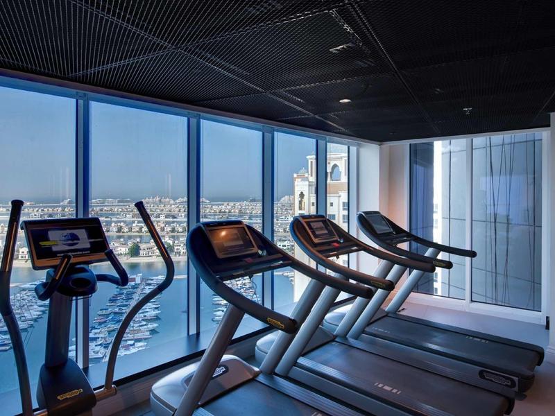 Moderne Fitnessraum mit Laufbändern und Ergometer vor großen Fenstern mit Stadtblick.