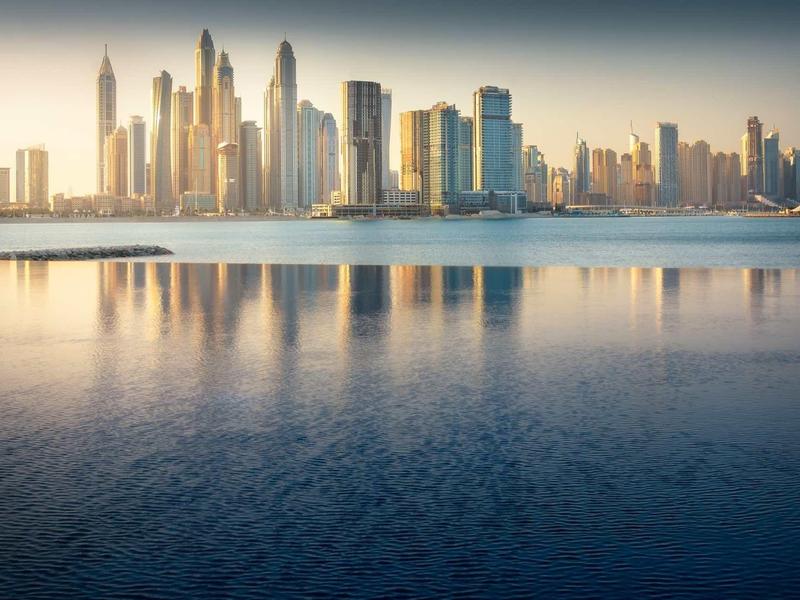 Stadtpanorama mit modernen Wolkenkratzern, Spiegelung im ruhigen Wasser bei Sonnenuntergang.