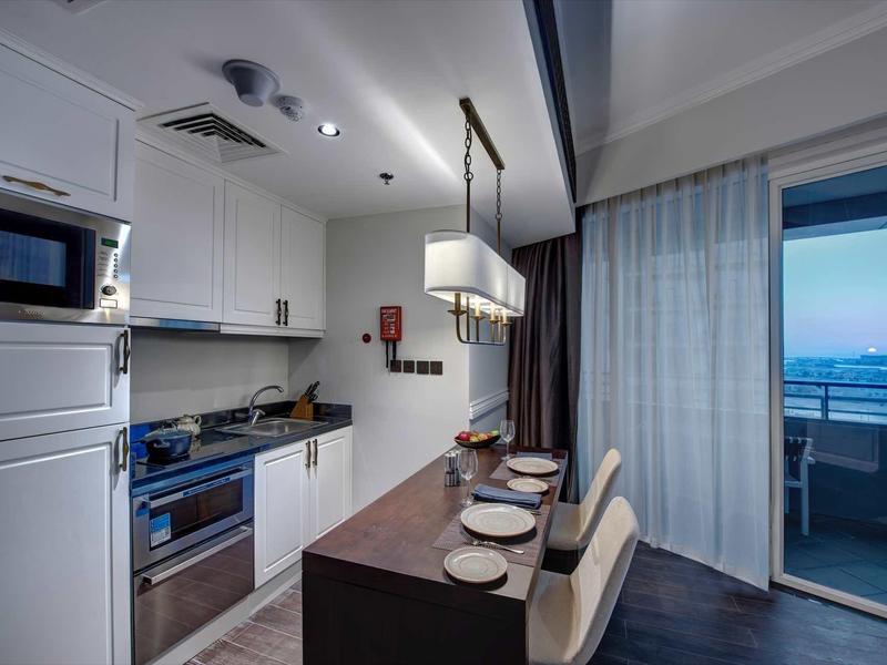 Moderne Küche mit weißer Einrichtung, Kochinsel, zwei Stühlen und Balkon mit Meeresblick bei Dämmerung.