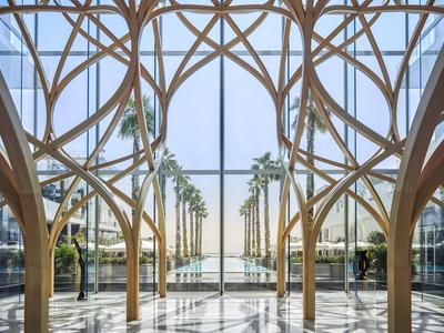 Widok przez elegancką nowoczesną drewnianą konstrukcję kolumnową na aleję z palmami i zbiornikami wodnymi.