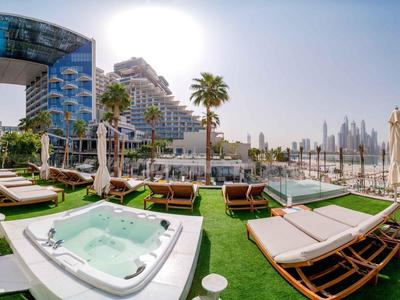 Moderner Hotelpoolbereich mit Liegestühlen, Whirlpool und Blick auf Hochhausarchitektur bei Sonnenschein.