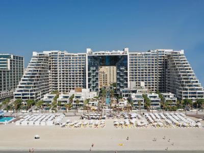 Großes modernes Hotel mit vielen Liegestühlen am Strand und klarem blauem Himmel.