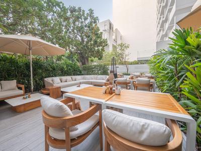 Nowoczesny taras z drewnianymi stołami, miękkimi krzesłami i parasolami obok zielonych roślin.