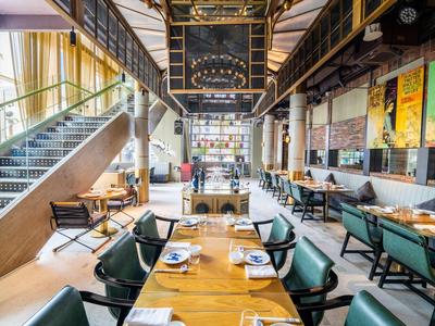 Modernes, stilvolles Restaurant mit langen Tischen, grünen Stühlen und industriellem Design.