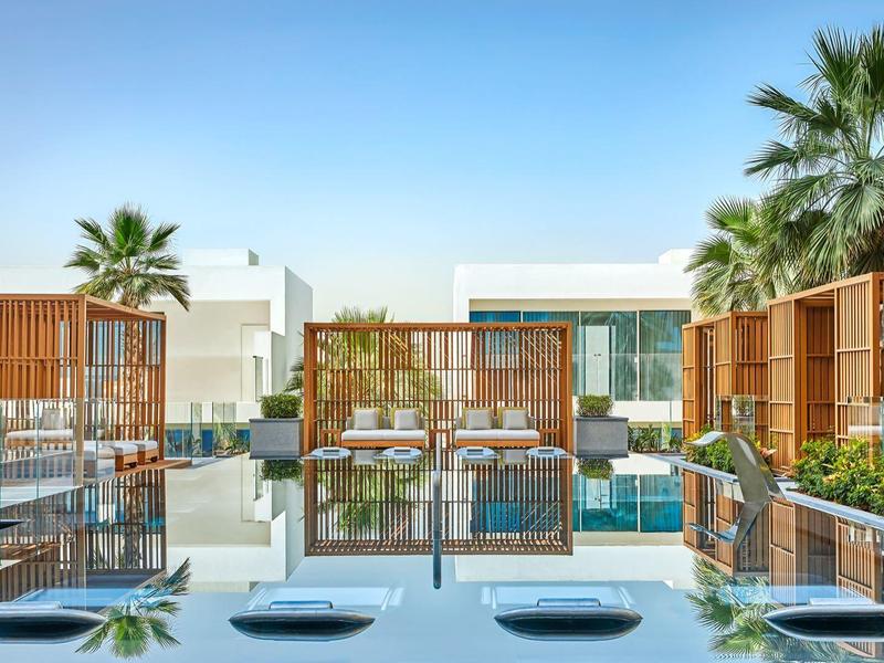 Moderner Hotelpool mit bequemen Liegen und Palmen unter klarem blauem Himmel.