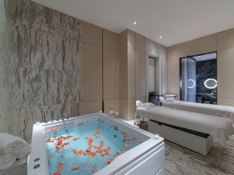 Moderner Hotel-Spa mit Whirlpool voller Blütenblätter und zwei Behandlungsliegen.