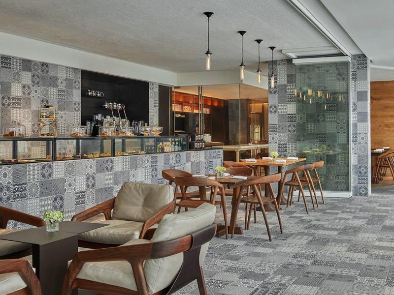 Moderner Aufenthaltsraum mit Holzstühlen und gemusterten Fliesen an der Barwand.