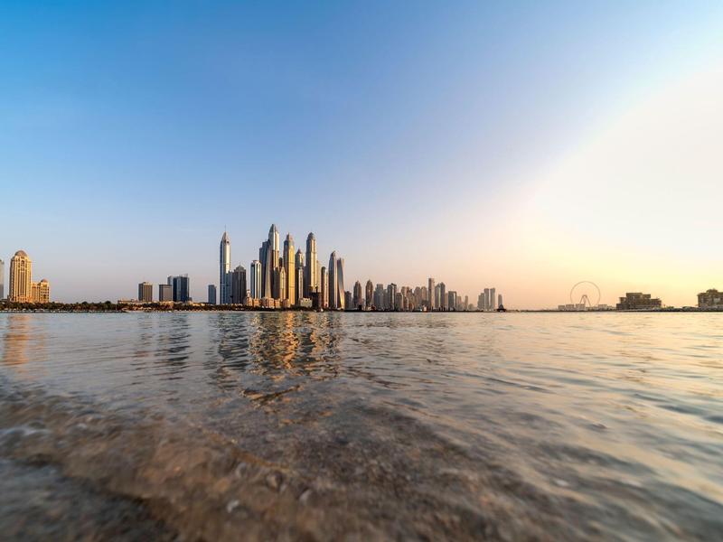 Blick vom flachen Ufer auf eine Skyline mit modernen Hochhäusern bei klarem Himmel