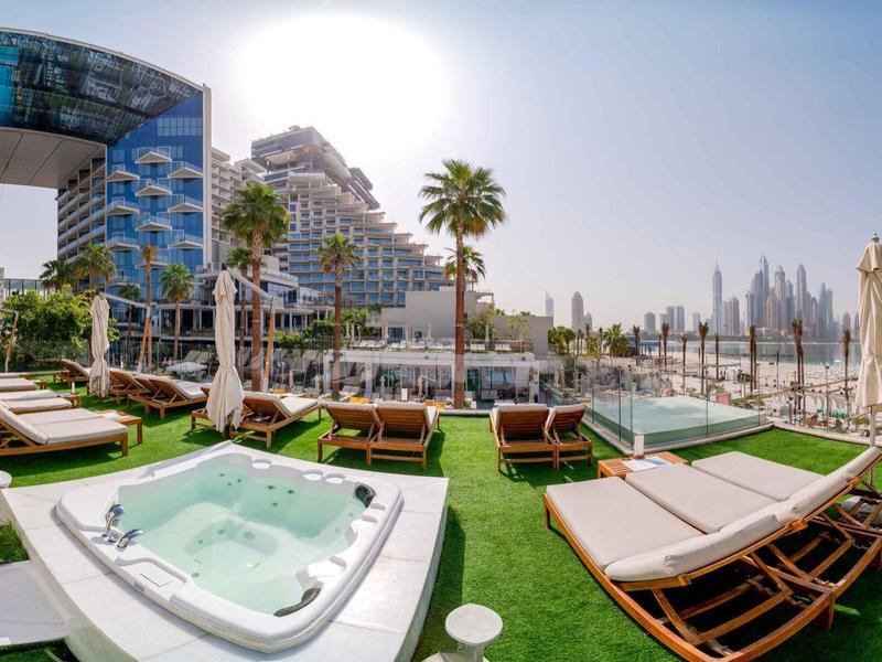 Moderner Hotelpoolbereich mit Liegestühlen, Whirlpool und Blick auf Hochhausarchitektur bei Sonnenschein.