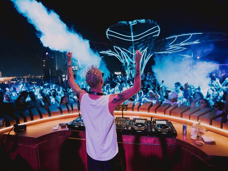 DJ legt in einem Club vor einer tanzenden Menge bei cooler Lichtshow auf.