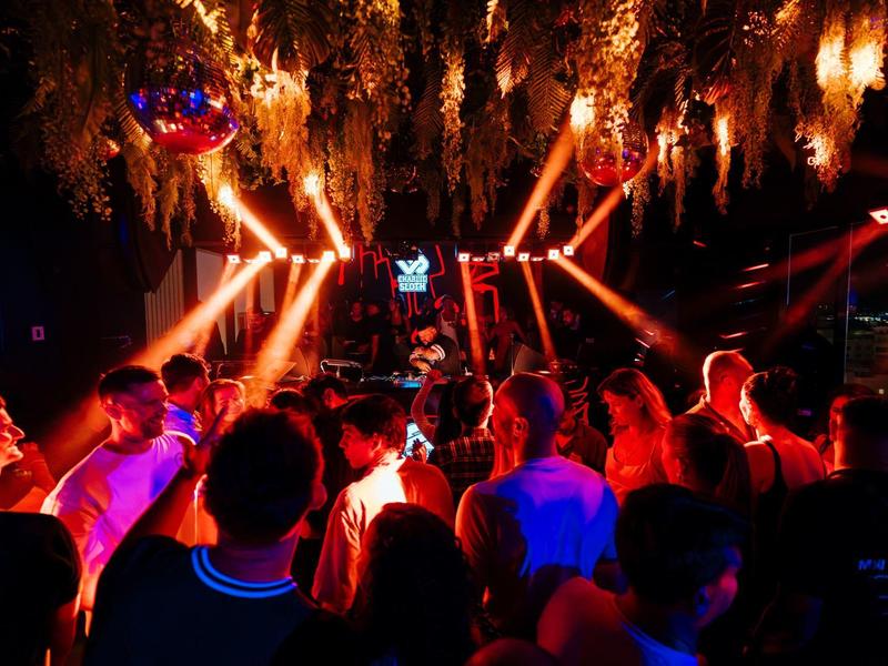 Menschen tanzen in einem dunklen Nachtclub mit bunten Lichtern und Effektstrahlern.