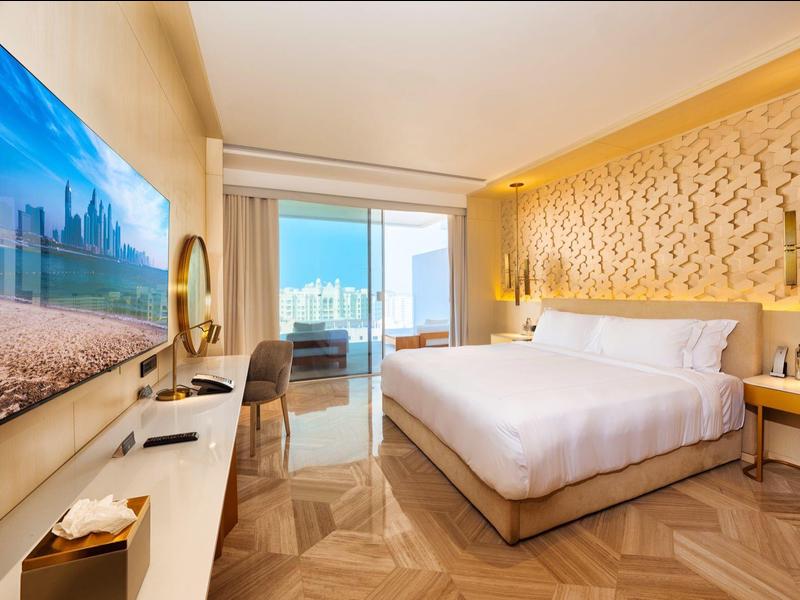 Modernes Hotelzimmer mit großem Bett, Fernseher und Balkon mit Meerblick.