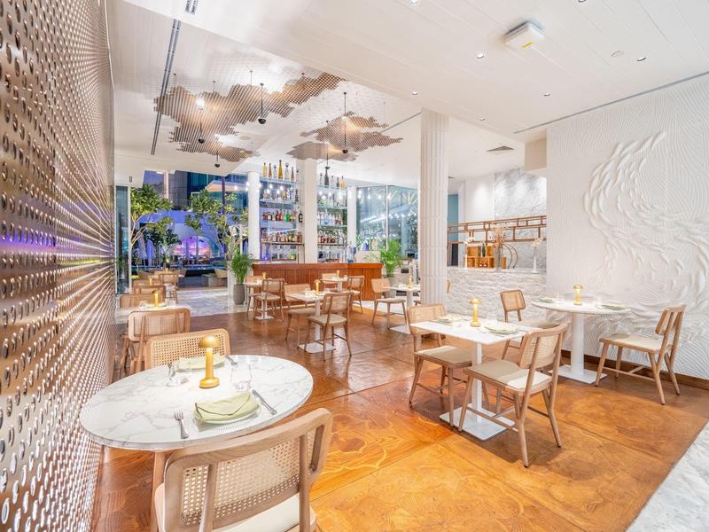 Modern eingerichtetes Restaurant mit Holzstühlen, weißen Tischen und dekorativen Wandelementen.