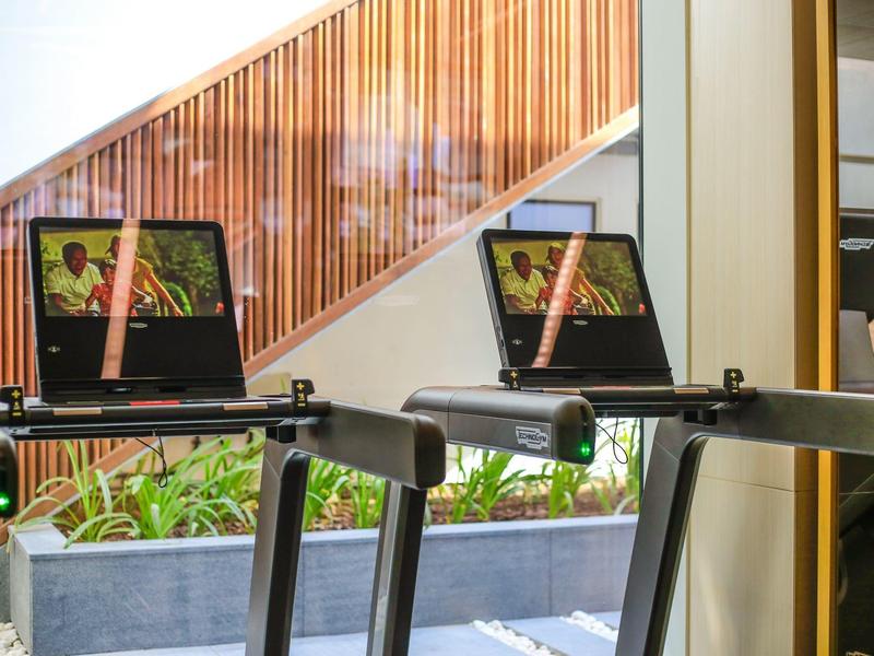 Zwei Laufbänder mit Fernsehern in einem modernen Fitnessraum mit Holzakzenten und Pflanzen.