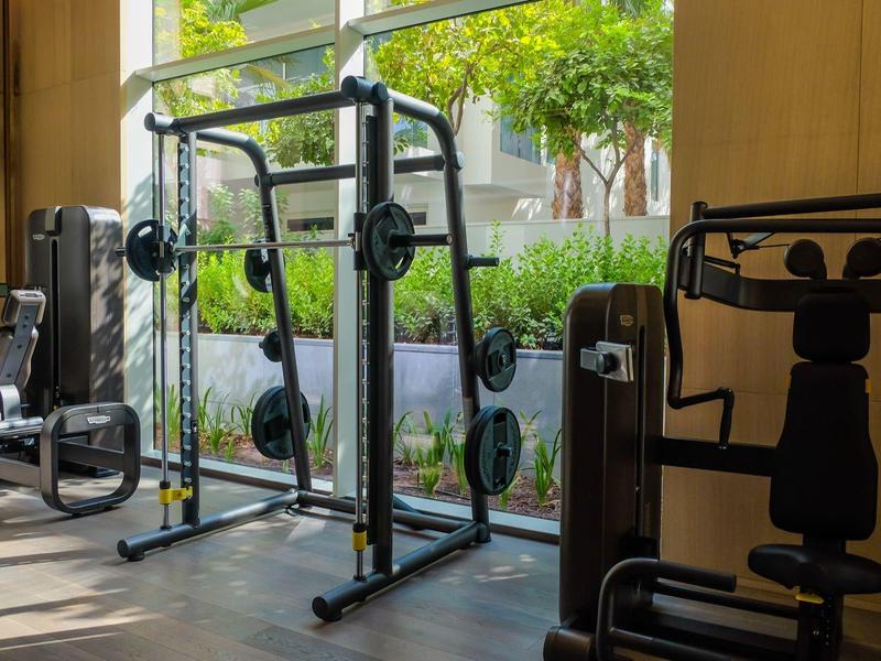 Fitnessraum mit Trainingsgeräten und großen Fenstern mit Blick ins Grüne.