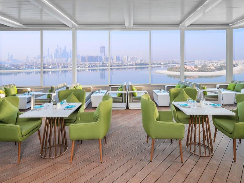 Heller, moderner Speisesaal mit grünen Sesseln, Holzböden und großen Fenstern mit Meerblick.