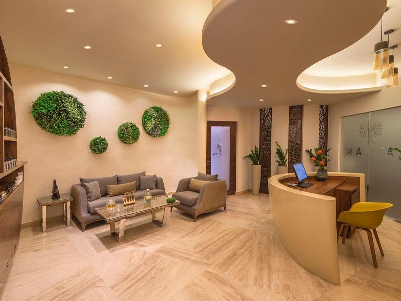 Moderne Lounge mit grauer Sitzecke, Holzregalwand, Pflanzen und geschwungener Decke mit Beleuchtung.