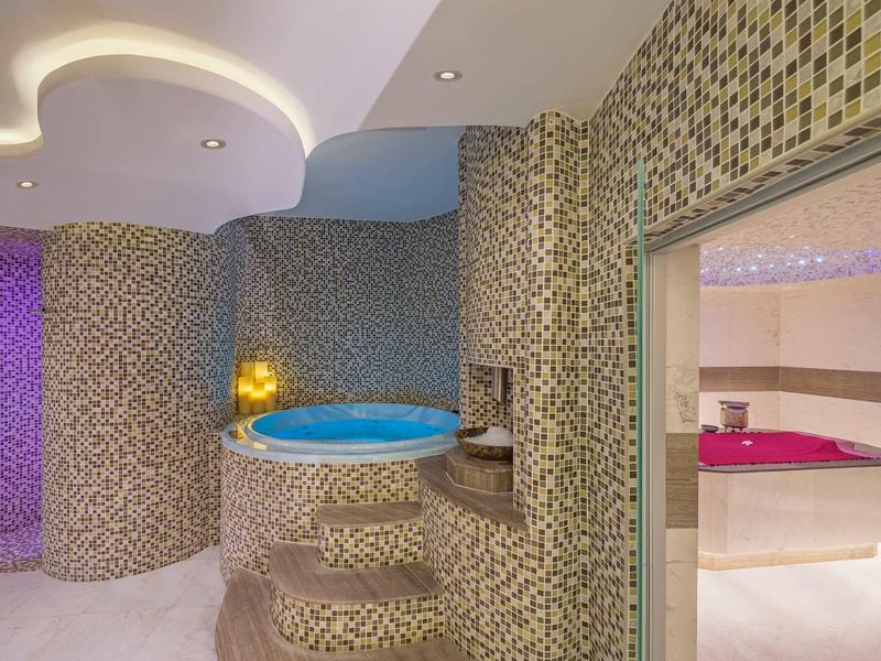Moderner Wellnessbereich mit rundem Whirlpool, Mosaikfliesen und angrenzendem Raum mit rosa Beleuchtung.