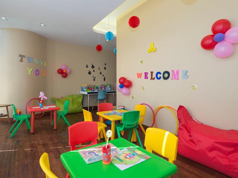 Bunter Kinderspielraum mit kleinen Tischen, Stühlen, Luftballons und ?Welcome?-Schrift an der Wand.