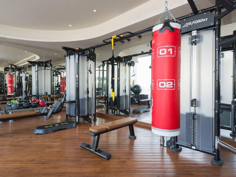 Moderner Fitnessraum mit Trainingsgeräte, Hanteln und rotem Boxsack auf Holzfußboden.