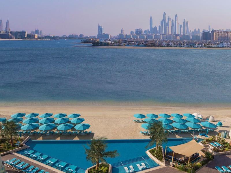 Blick auf einen Strand mit Liegestühlen und Sonnenschirmen, Skyline einer Stadt im Hintergrund