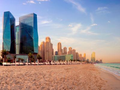 Ein breiter Sandstrand mit Menschen, hoch aufragende Wolkenkratzer und ein blauer Himmel bei Sonnenuntergang.