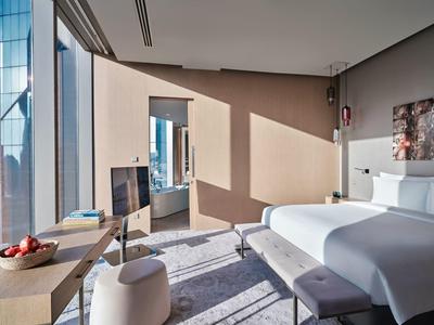 Modernes Hotelzimmer mit großem Bett, hellem Holz, Glasfenstern und Sitzbereich, sonnendurchflutet.