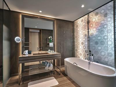 Modernes Badezimmer mit freistehender Badewanne, großem Spiegel und eleganter Wandverkleidung.