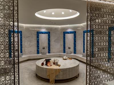 Eleganter Hamam mit rundem Marmorbecken, Sitzbänken und filigranen Trennwänden.