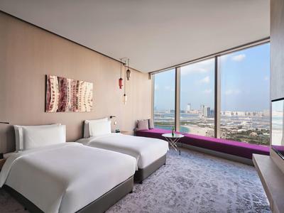 Modernes Hotelzimmer mit zwei Betten, großem Panoramafenster und Stadtblick, helle Farben, Teppichboden.