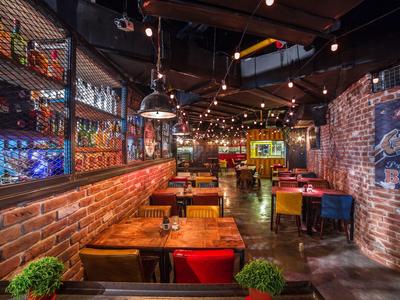 Gemütliche Bar mit roter Backsteinwand, Holztischen, bunten Sitzbänken und warmen Lichterketten.