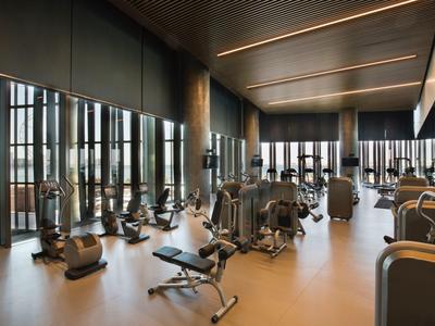 Großzügiger Fitnessraum mit modernen Geräten, großen Fenstern und gedämpftem Holzambiente.