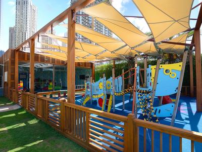 Kinder-Spielplatz mit bunten Klettergerüsten, gelben Segeln und umgeben von Holz.