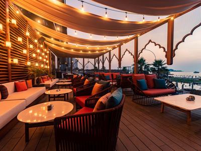 Elegante Lounge mit warmem Licht, Holzdecke, gemütlichen Sitzgruppen und Blick auf den Sonnenuntergang.