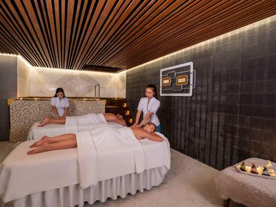 Ein Spa-Raum mit dunklen Wänden, Holzdecken und zwei Frauen, die Massagen geben.