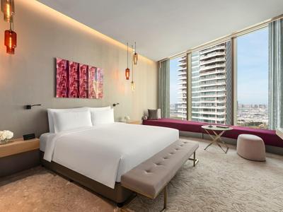 Habitación de hotel moderna con cama grande, ventanales panorámicos y muebles elegantes con vista a la ciudad.