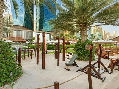 Outdoor fitness area with equipment surrounded by palm trees and urban backdrop.