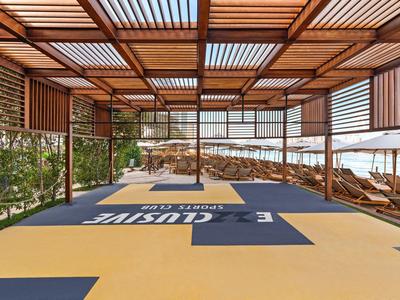 Covered wooden lounge area with sunbeds and sea view at hotel pool