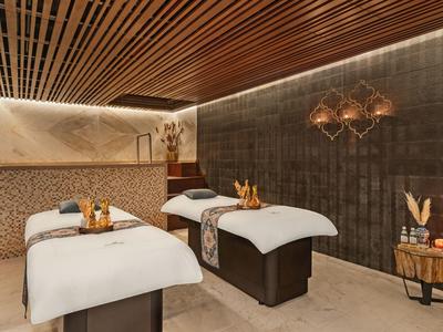 Sala de spa elegante con dos camillas, luz cálida y decoración moderna de madera.