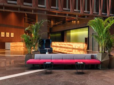 Modern hotel lobby with red sofa, green plants, and stylish lighting.