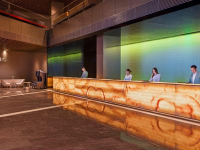 Moderner Hotel-Empfangsbereich mit beleuchtetem Onyx-Tresen und Personal hinter der Rezeption.