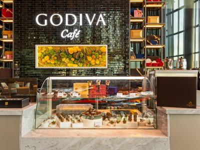 Moderne Cafétheke mit Schokoladendesserts und dekorativem Godiva-Café-Logo an der Wand.