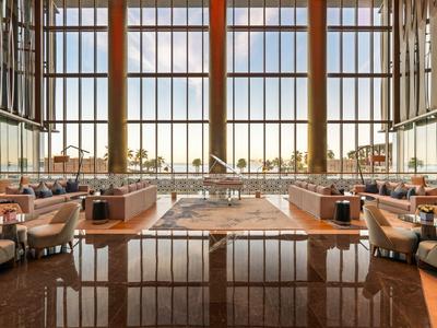 Innenraum eines modernen Hotels mit hohen Fenstern, Sitzbereichen und Blick ins Freie.