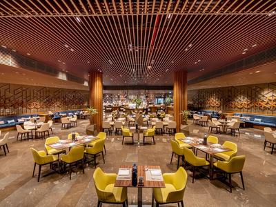 Geräumiges Hotelrestaurant mit gelben Sesseln und hölzernen Deckenbalken.