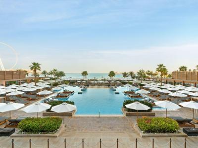 Großer Pool mit weißen Sonnenschirmen und Liegen in einem Luxushotel am Meer.