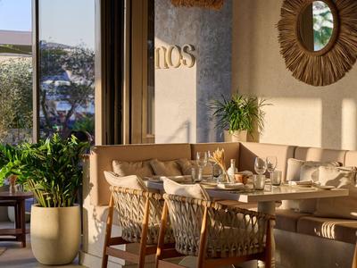 Helles Hotelrestaurant mit Holzmöbeln, Pflanzen und sonnigem Ausblick.